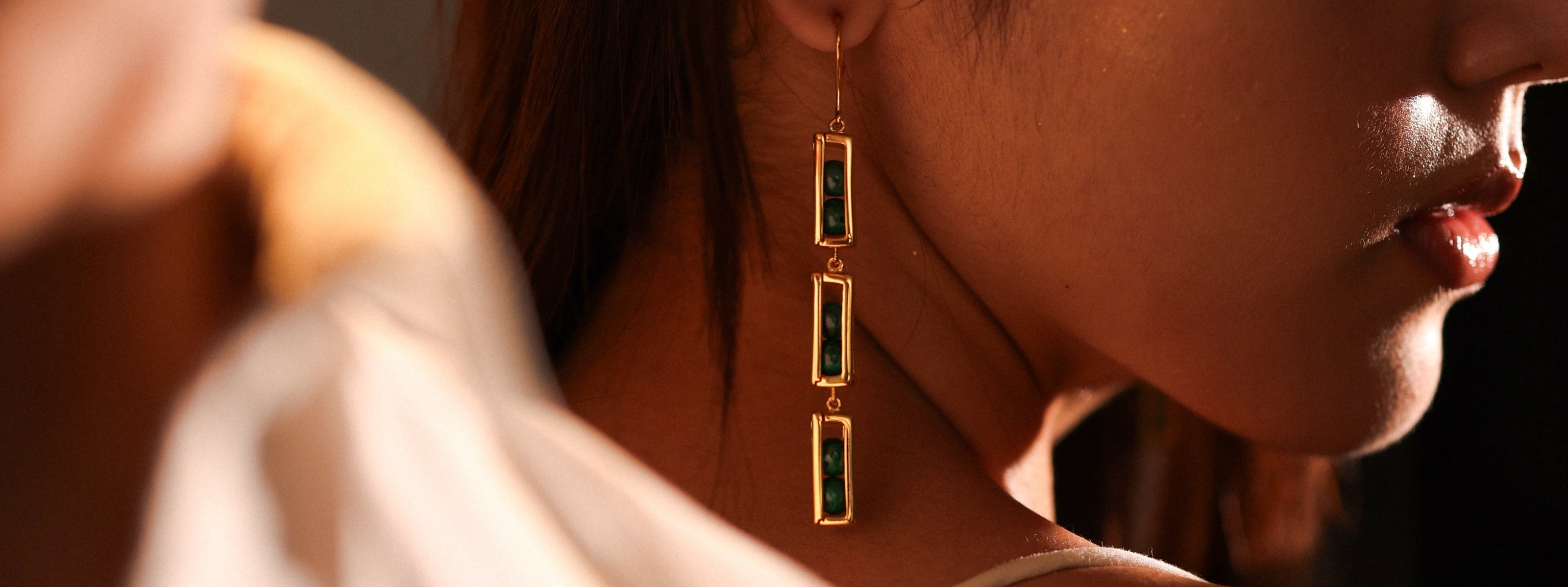 Model wearing Mhari Deewani long drop earrings with green stones in gold-plated silver
