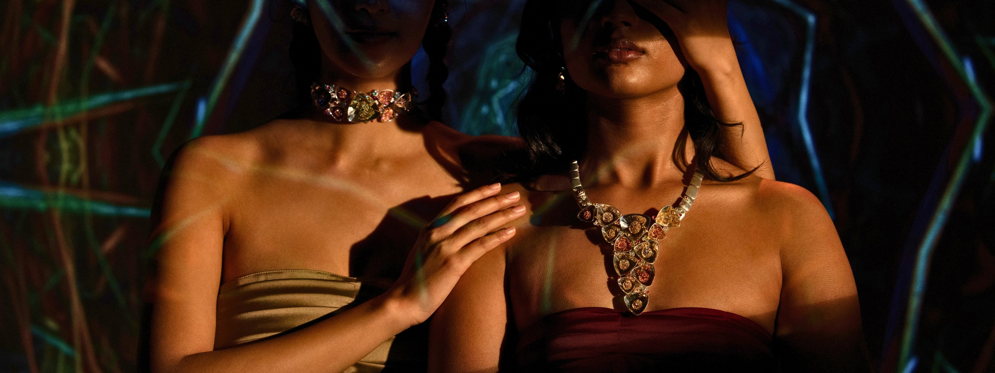 Two models in jewel-toned light wearing Mhari Maharani gemstone statement necklaces in gold-plated silver