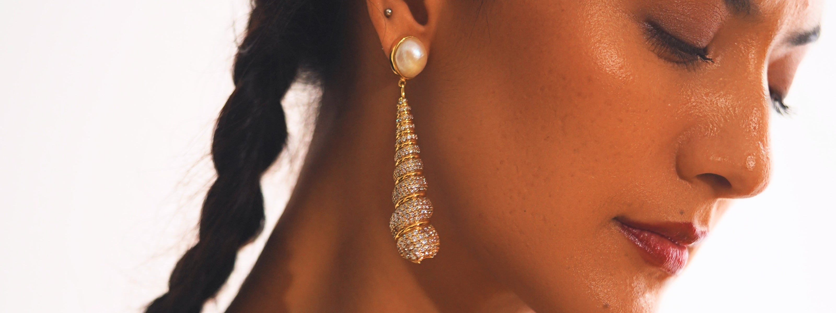 Model in profile wearing a Mhari pavé spiral drop earring with a pearl top in gold-plated silver