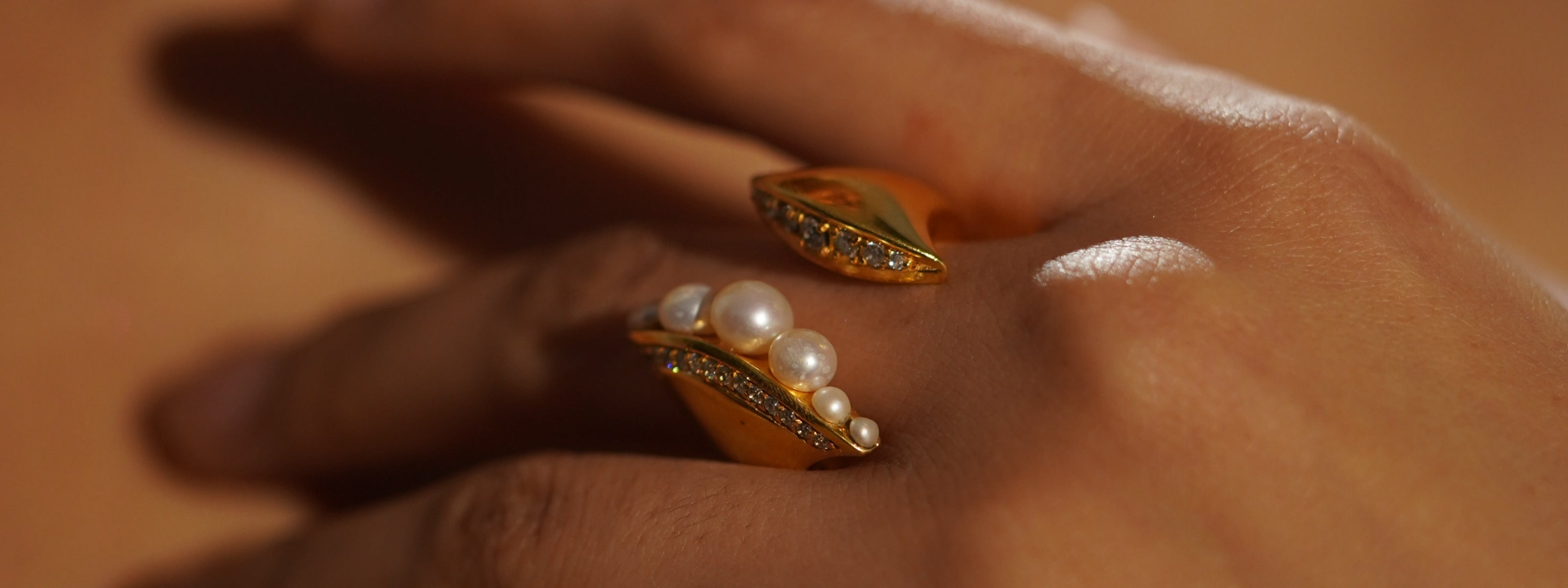 Two Mhari gold-plated silver rings with pearls and pavé stones worn on a hand