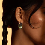 Aeris abalone labradorite teardrop earring worn in profile close-up against warm golden background.