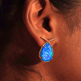 Aeris vivid blue opal teardrop statement earring worn close to ear on model in warm editorial shot.