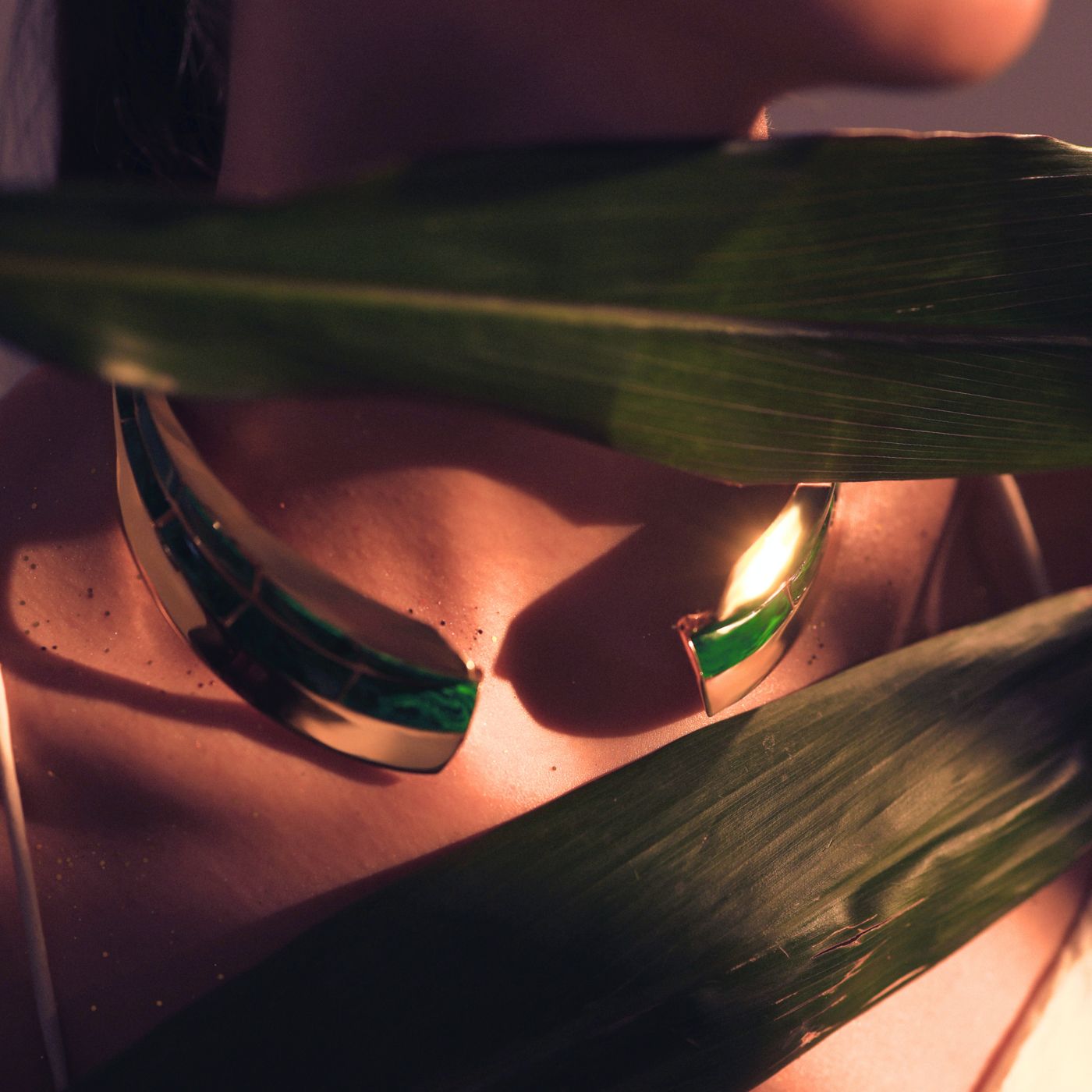 Model wearing malachite collar necklace and earrings partially obscured by tropical leaf