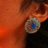 Close-up of blue opal spiral earring on model's ear in dark warm lighting