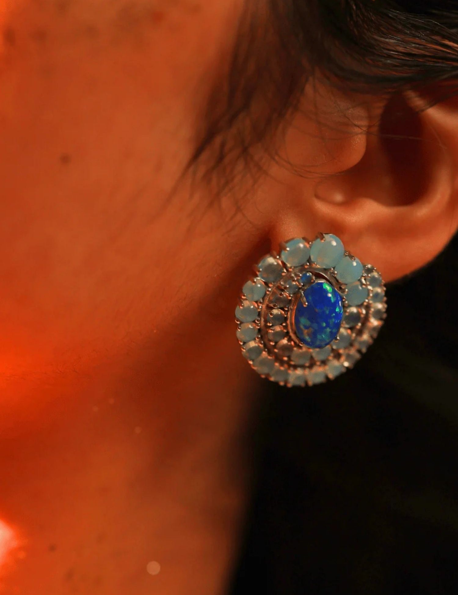 Close-up of blue opal spiral earring on model's ear in dark warm lighting