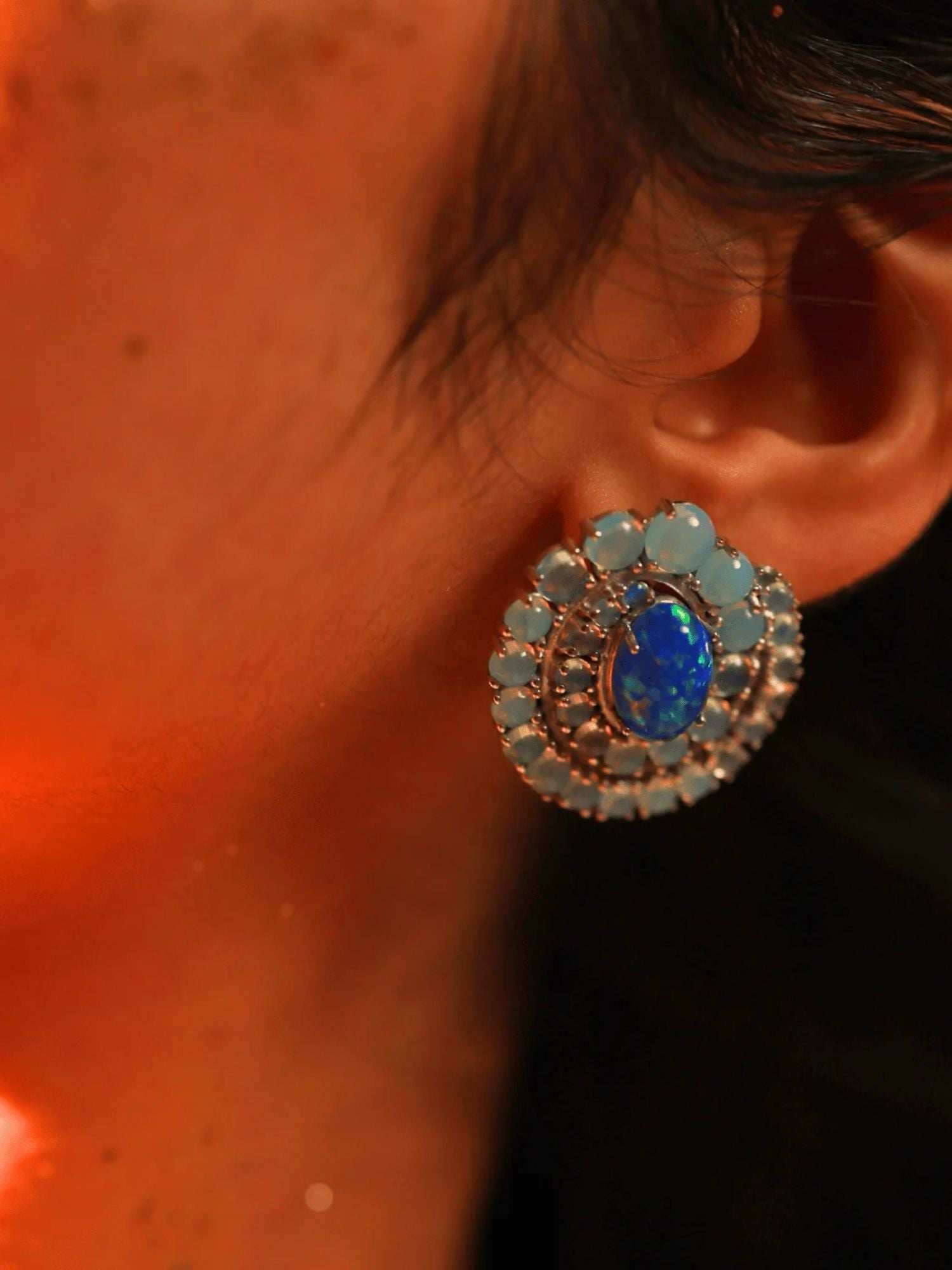 Close-up of blue opal spiral earring on model's ear in dark warm lighting
