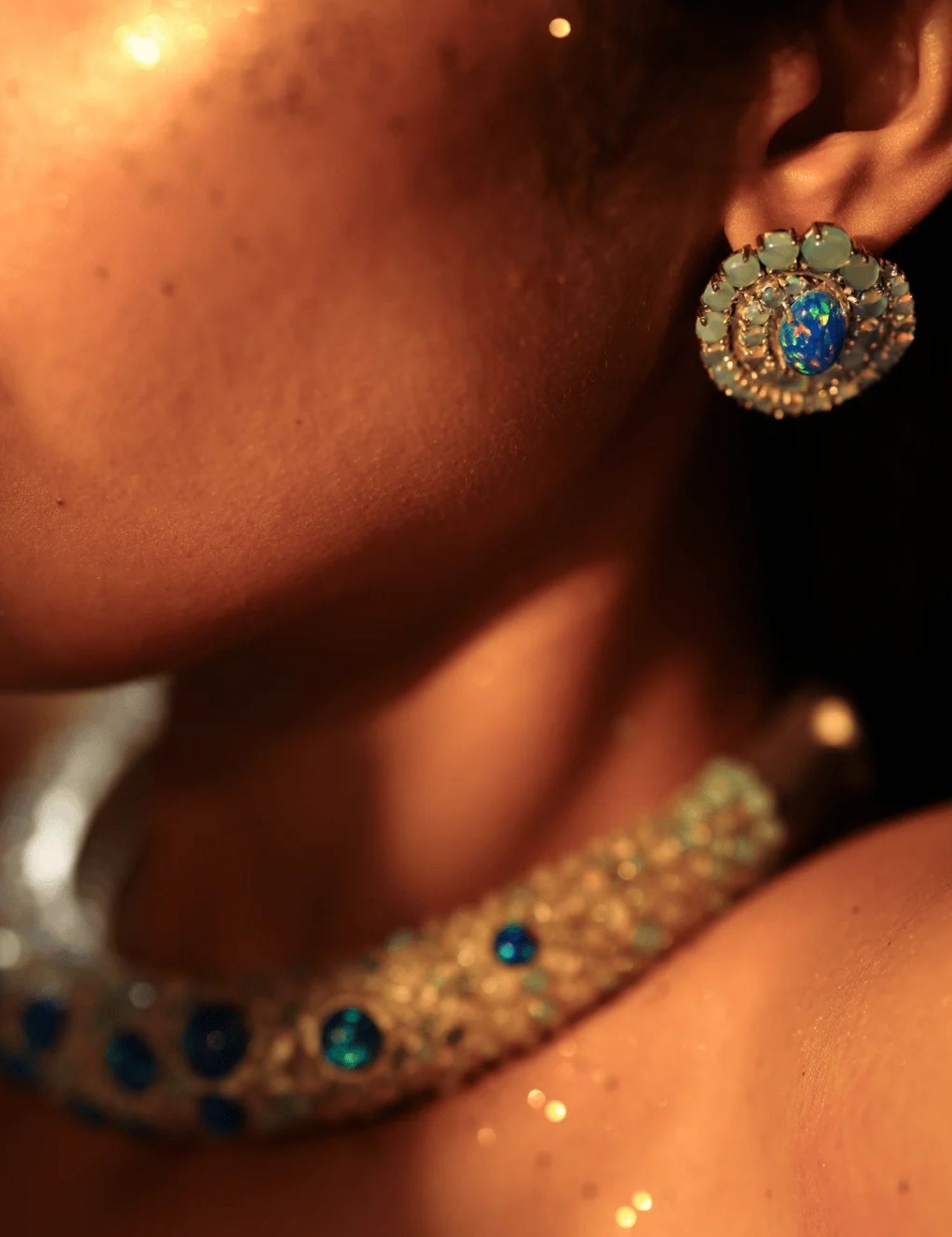 Model wearing blue opal spiral earrings with hasli necklace in warm ambient light