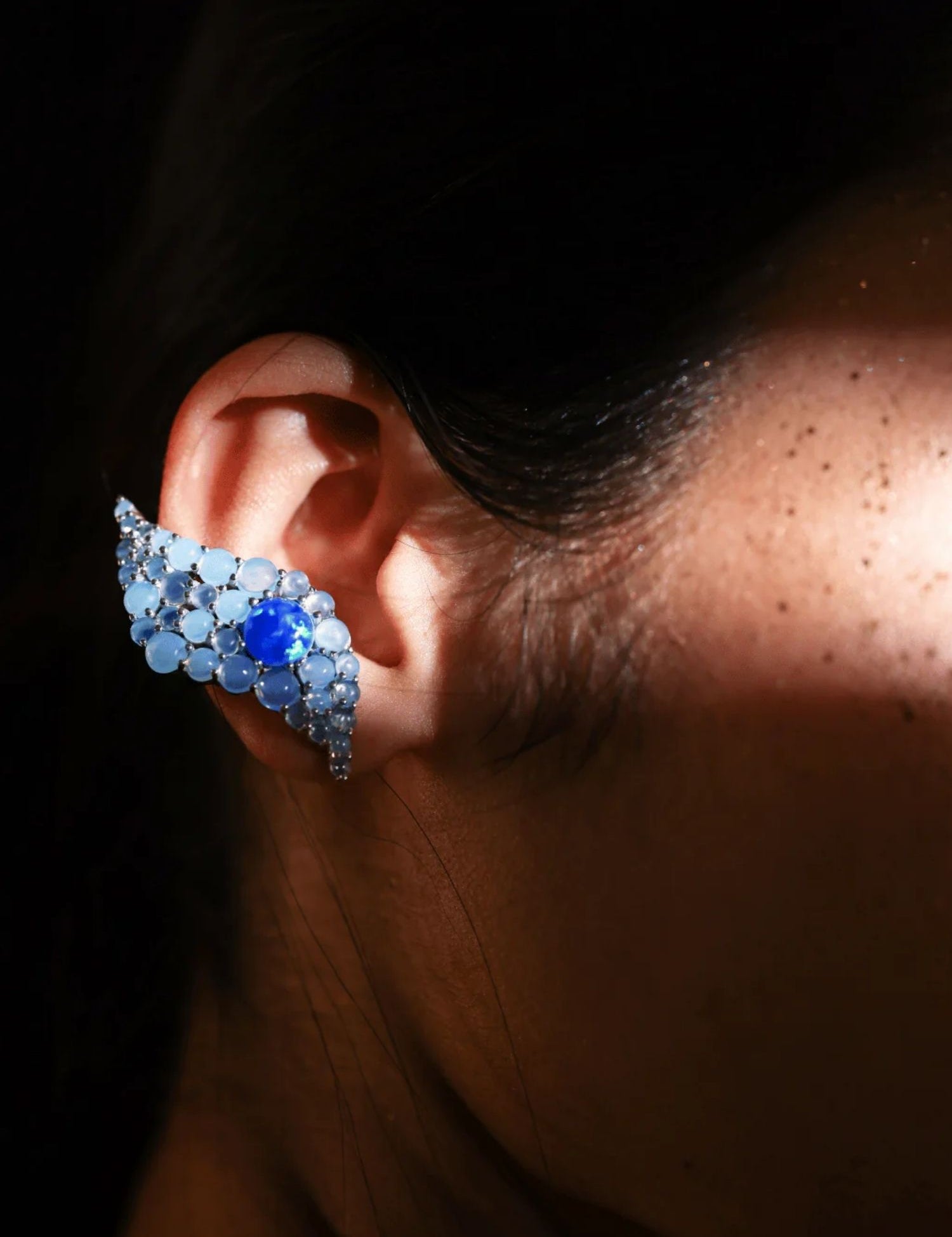 Side profile of model wearing blue opal wave ear cuff in low natural light
