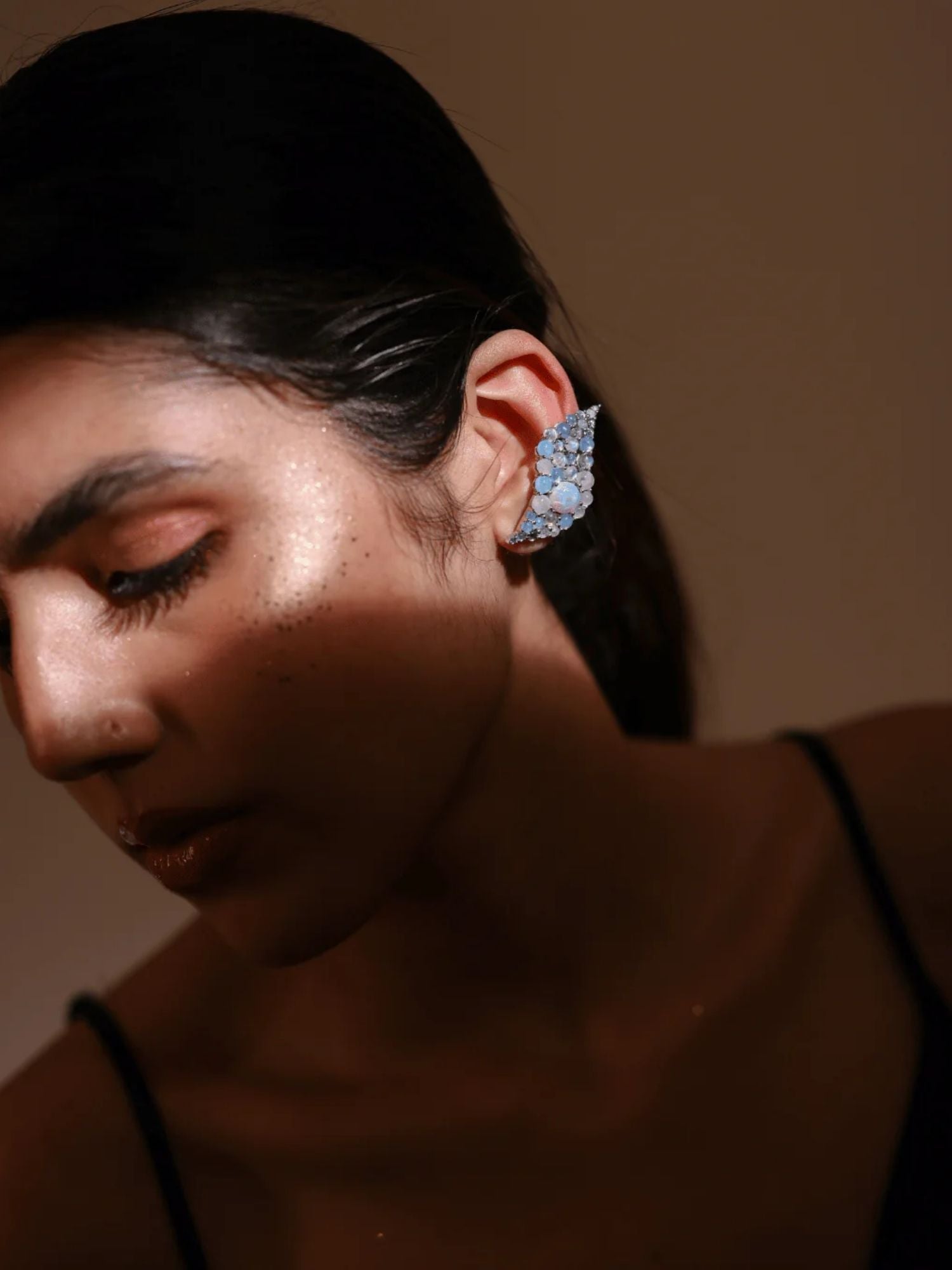 Model wearing blue opal wave ear cuff, eyes closed, warm ambient light