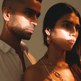 Model wearing large gold claw earrings in couple portrait, warm outdoor light