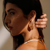 Close-up of large gold claw earring on model's ear with chain necklace visible