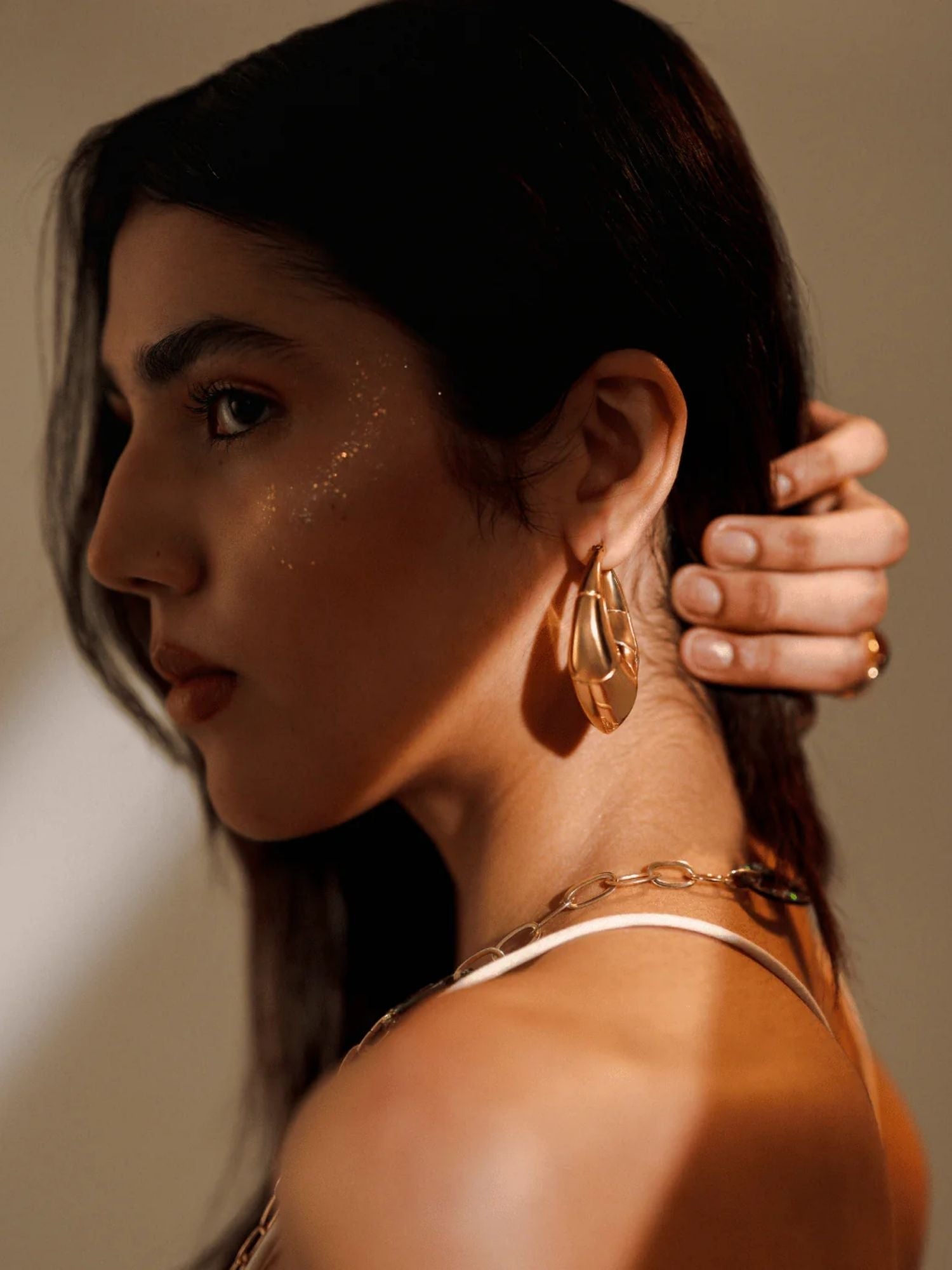 Close-up of large gold claw earring on model's ear with chain necklace visible