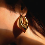 Model wearing large gold claw earring, close-up side profile in warm light