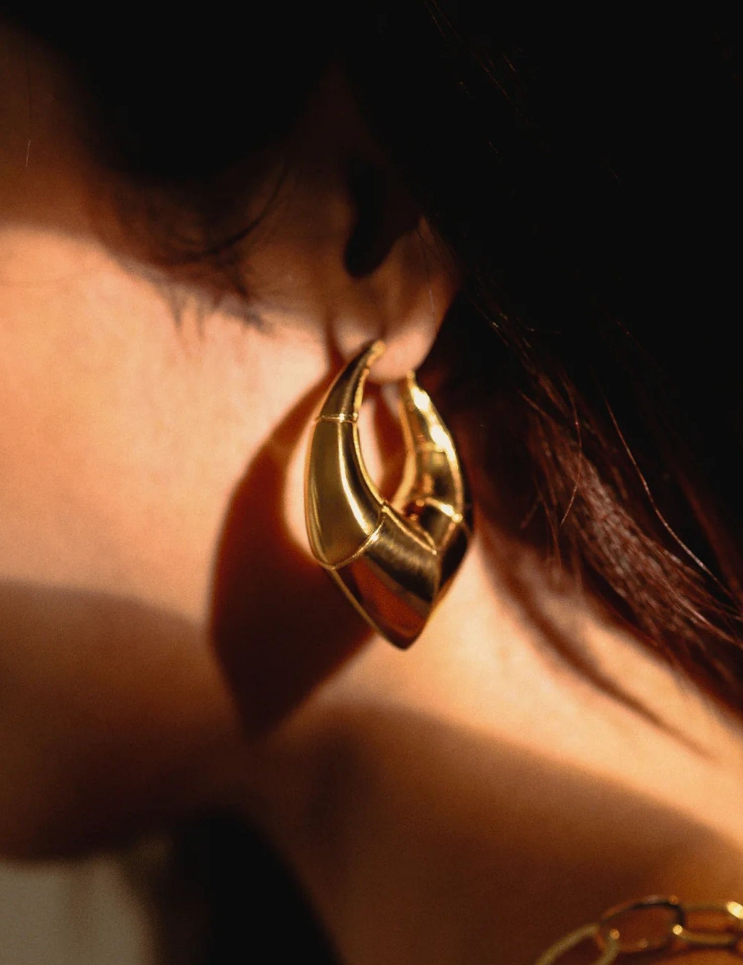 Model wearing large gold claw earring, close-up side profile in warm light