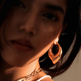 Model in close portrait wearing oversized gold claw earrings, dramatic lighting