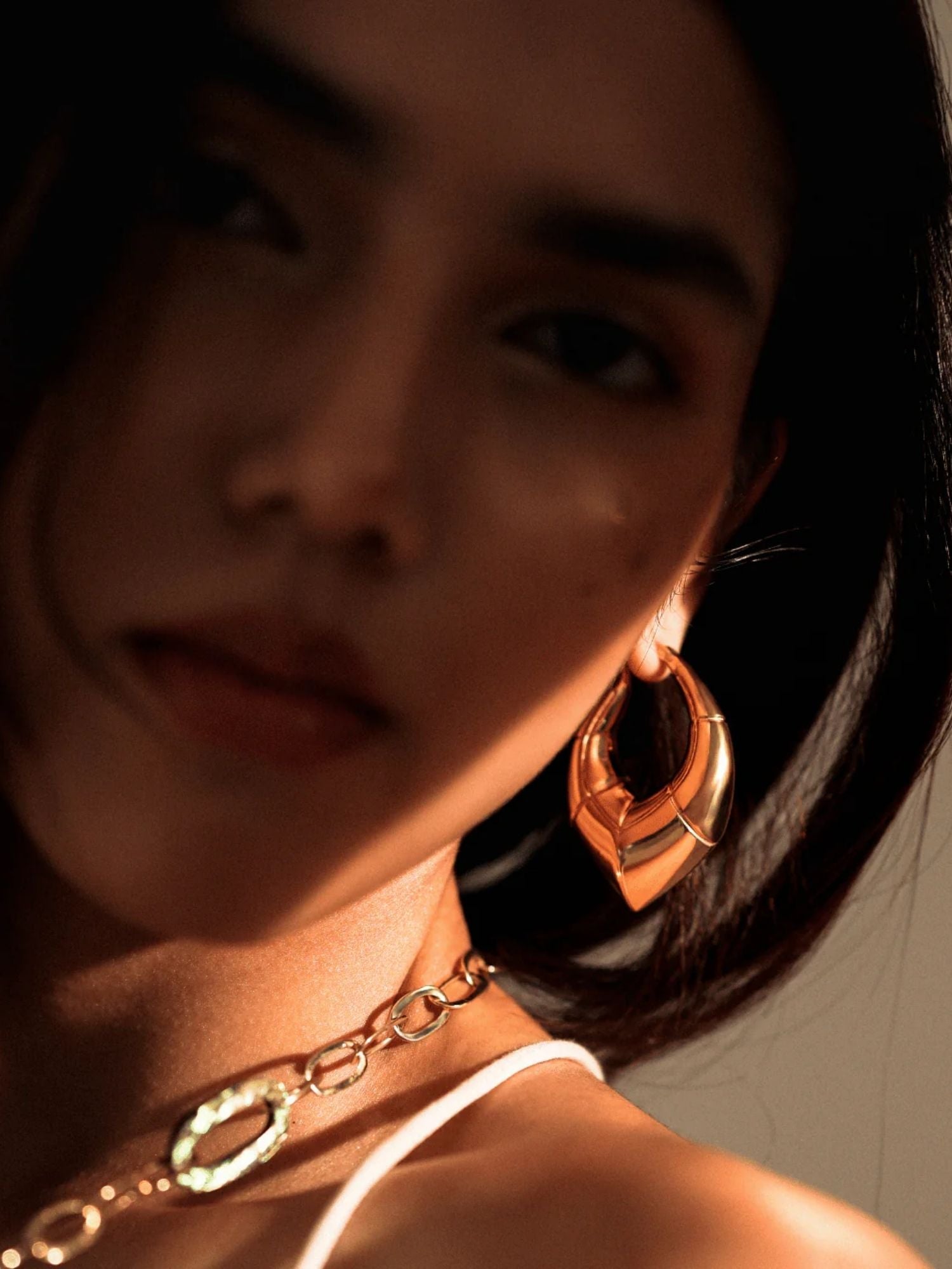 Model in close portrait wearing oversized gold claw earrings, dramatic lighting