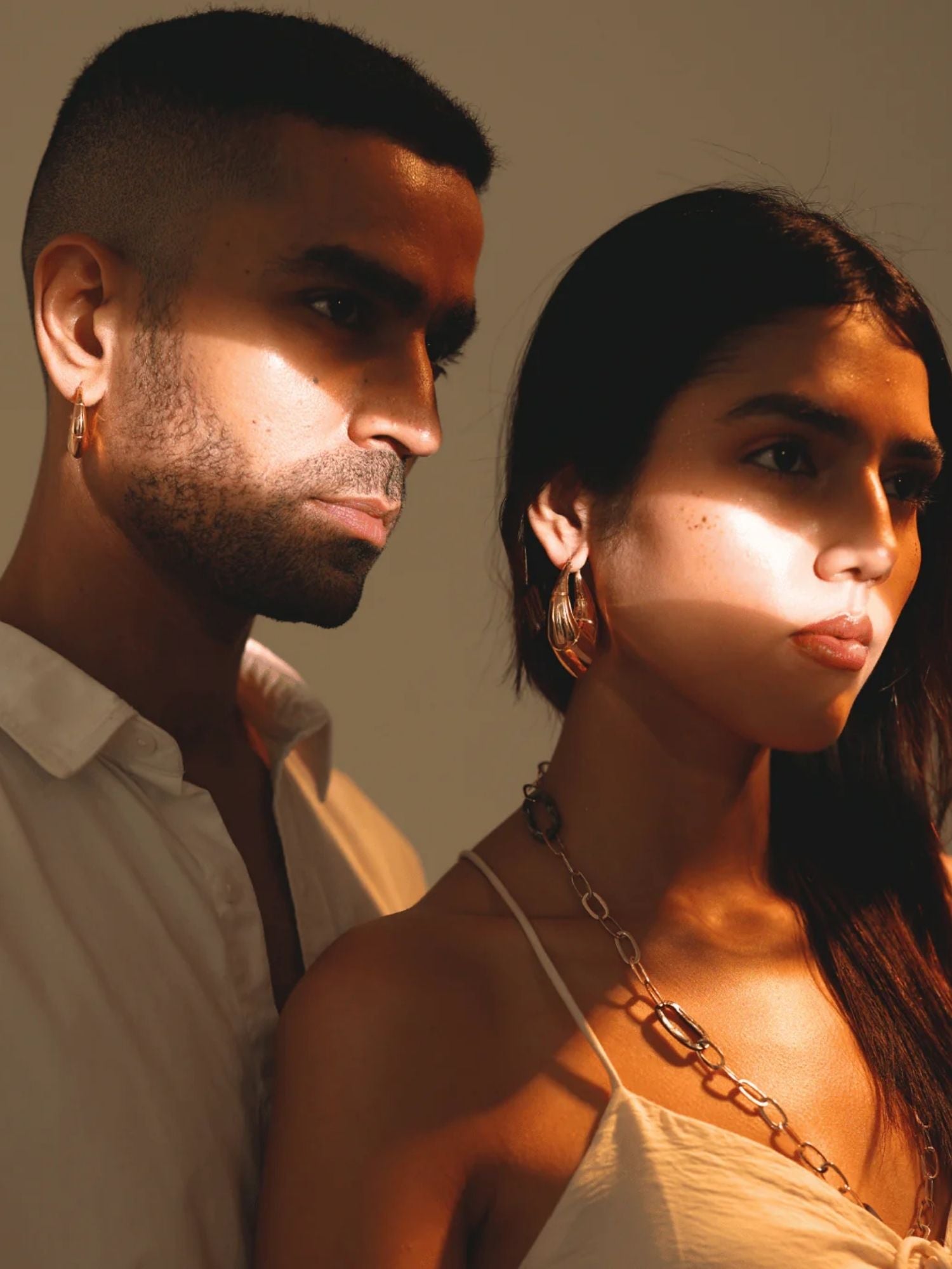 Model wearing small gold claw earrings in couple portrait, outdoor warm light