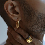 Close-up of male model wearing gold claw earring with ring visible on hand