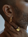 Close-up of male model wearing gold claw earring with ring visible on hand