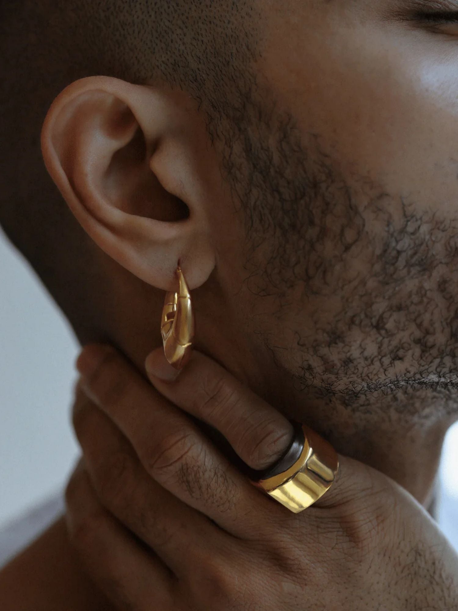 Close-up of male model wearing gold claw earring with ring visible on hand
