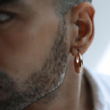 Male model wearing small gold claw earring, side profile outdoor portrait