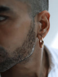 Male model wearing small gold claw earring, side profile outdoor portrait