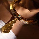 Close-up of gold collar necklace on model's collarbone showing surface finish and green stone
