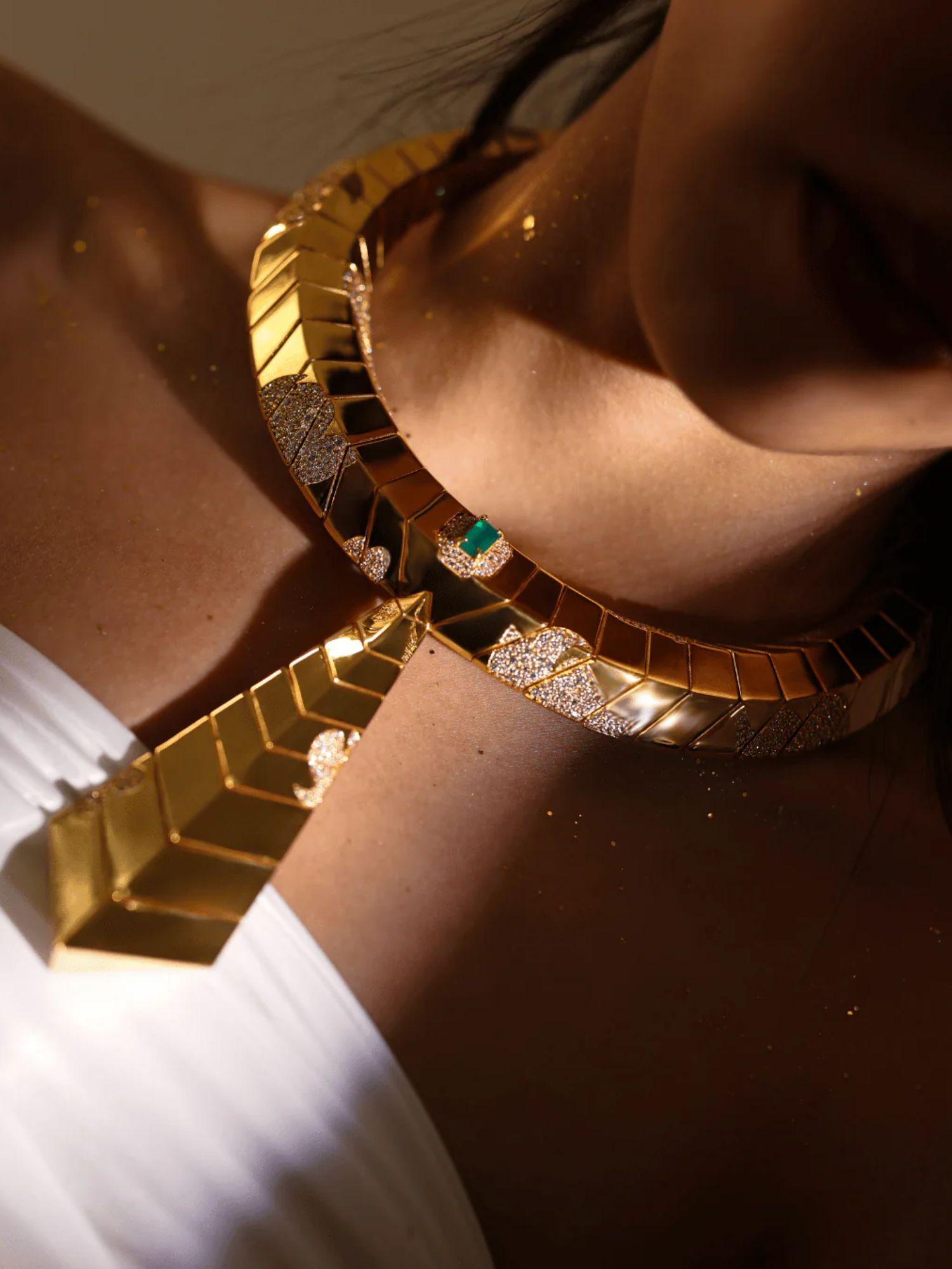 Close-up of gold collar necklace on model's collarbone showing surface finish and green stone