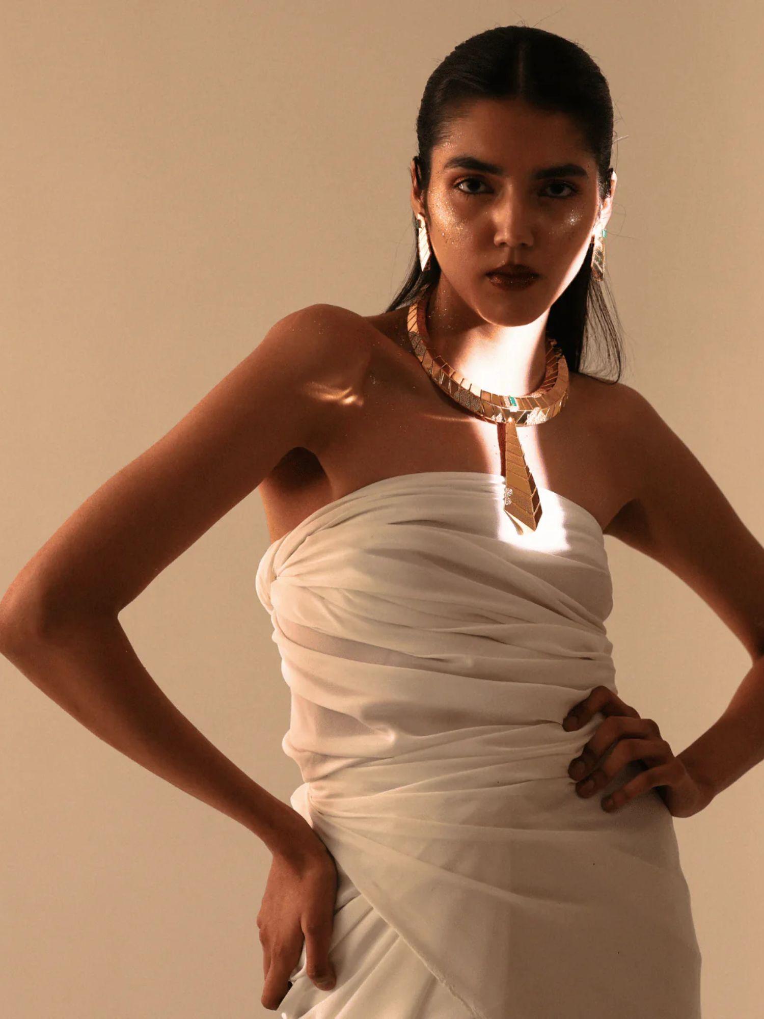 Full-body model shot in white dress wearing gold collar necklace with tie pendant
