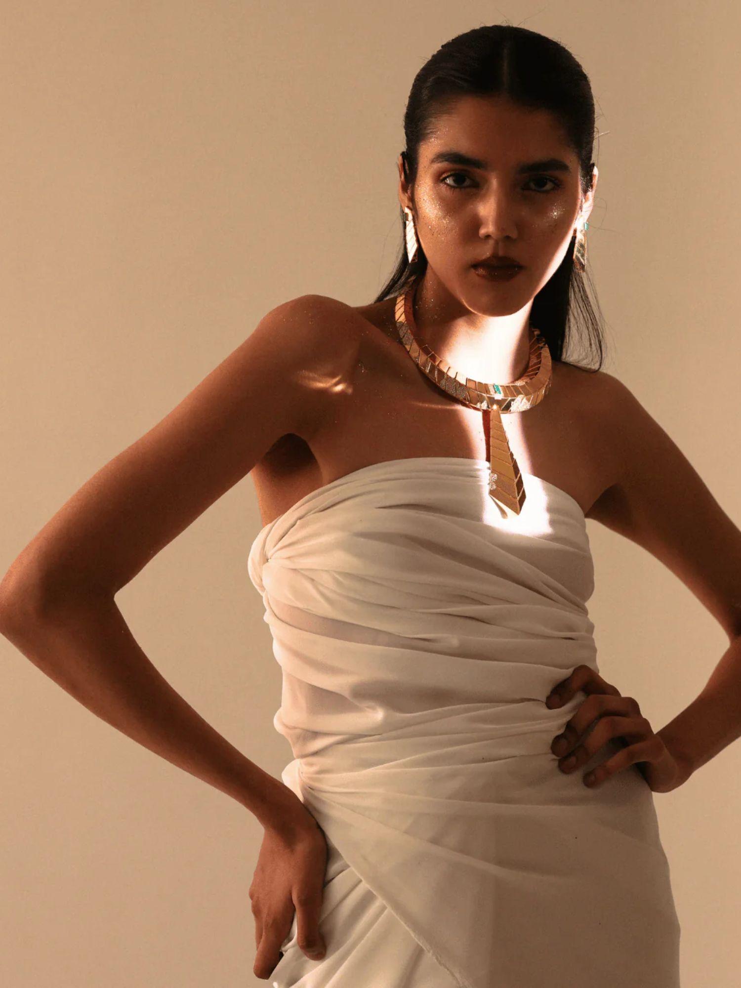 Model in white dress wearing sculptural gold collar necklace with tie pendant