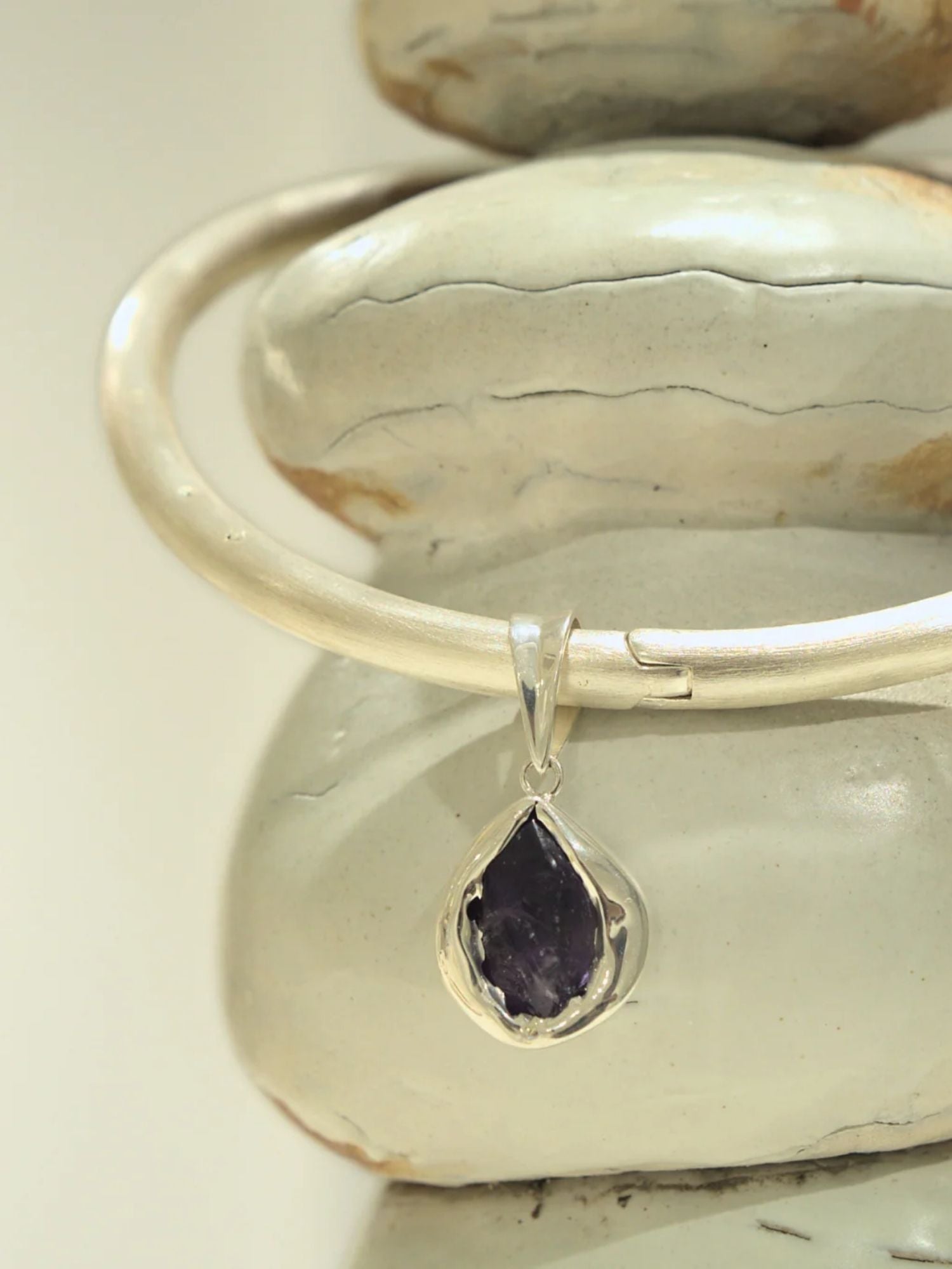 Silver bangle choker with raw agate teardrop charm resting on clay prop