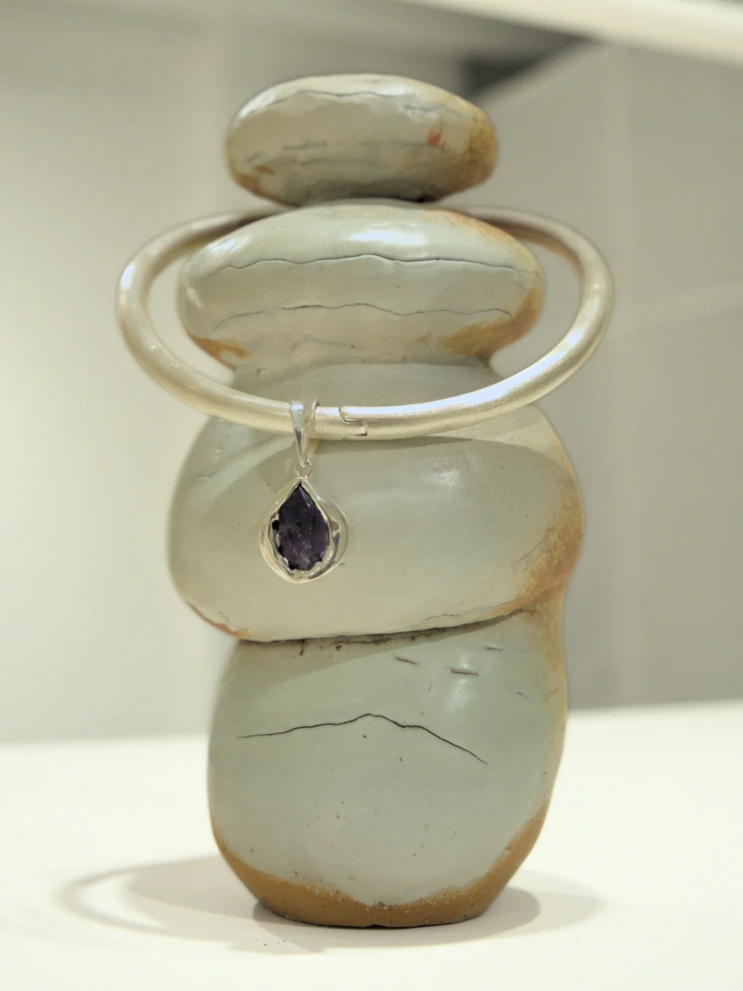 Silver bangle choker with black agate teardrop charm on stacked stone prop