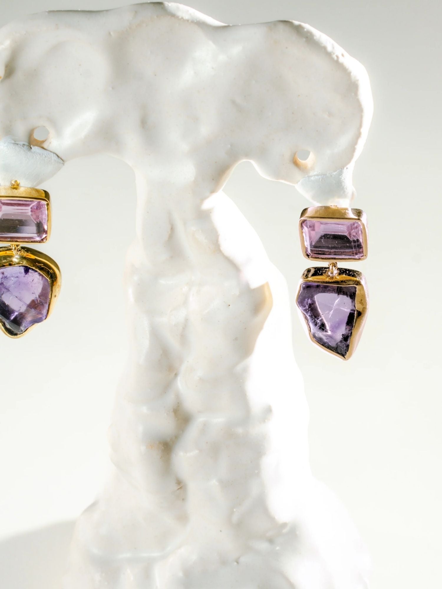 Close-up of gold amethyst and raw stone drop earrings on white prop