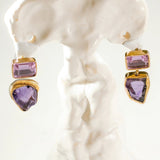 Gold amethyst drop earrings with raw stone charm on white sculptural prop