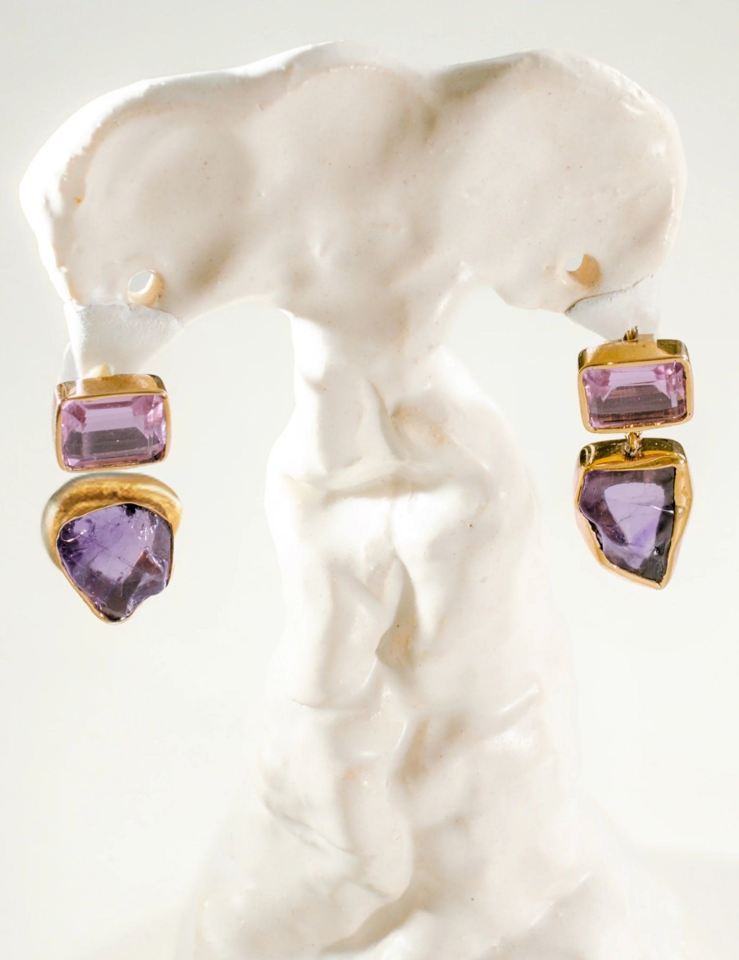 Gold amethyst drop earrings with raw stone charm on white sculptural prop