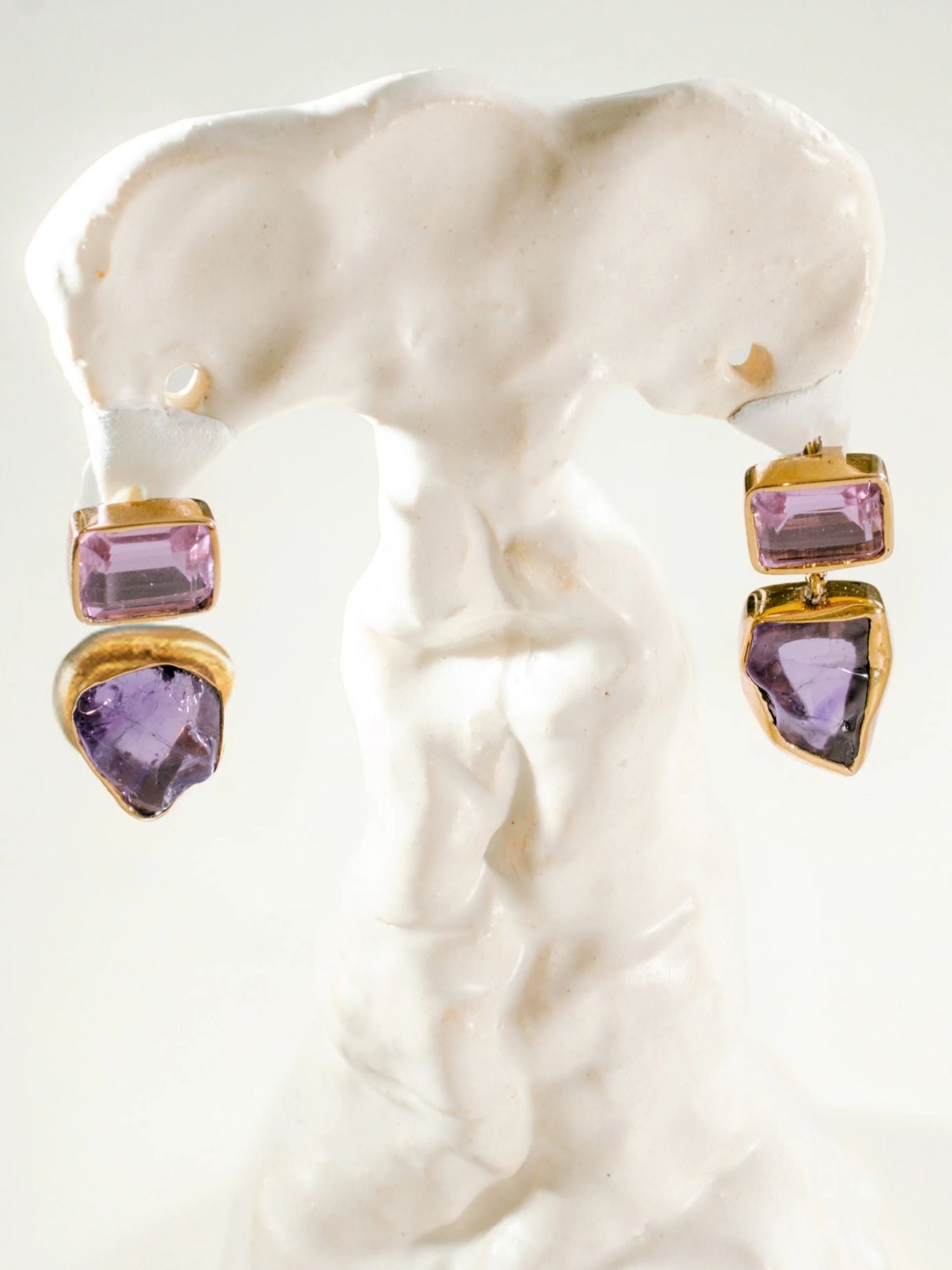 Gold amethyst drop earrings with raw stone charm on white sculptural prop