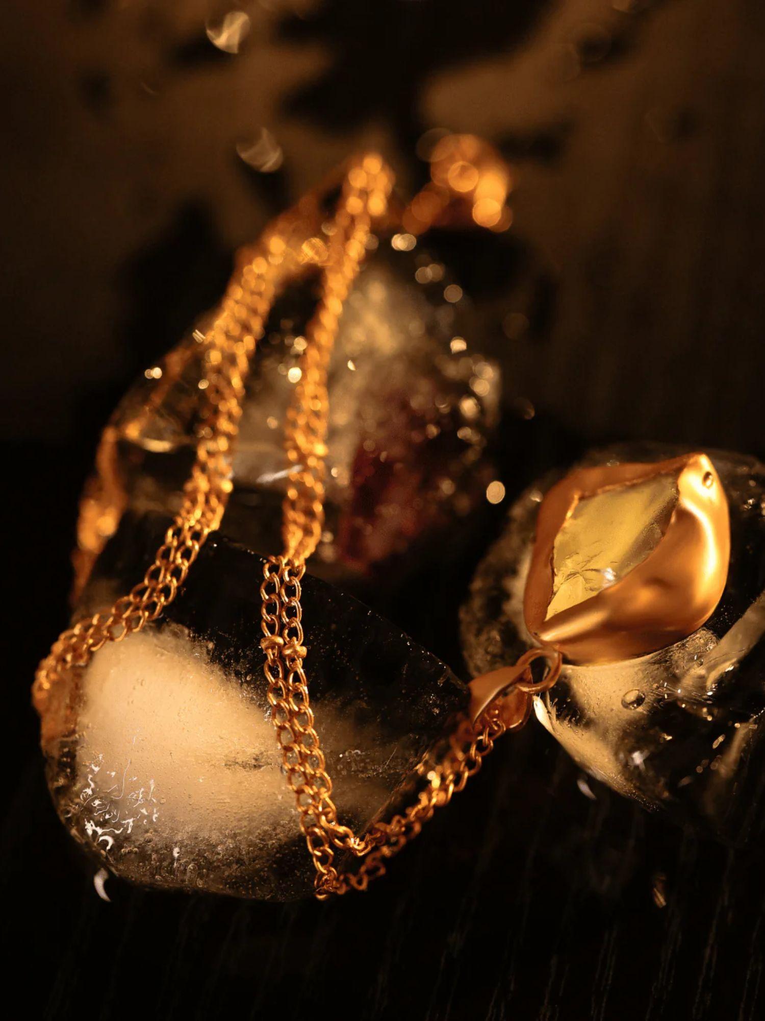 Raw stone gold pendant necklace draped over ice in dark editorial lighting