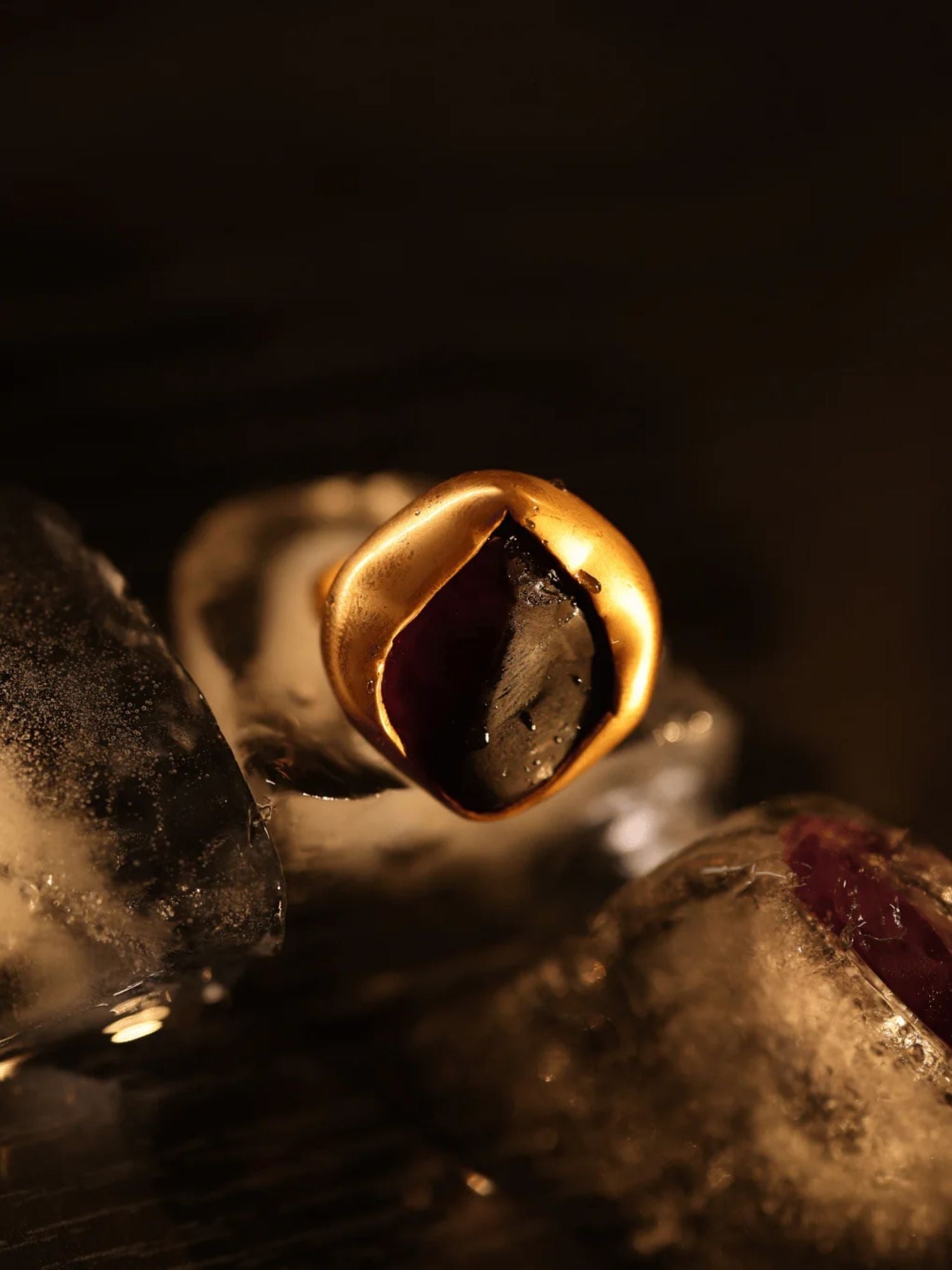 Gold raw agate cocktail ring held over ice, dramatic dark editorial shot