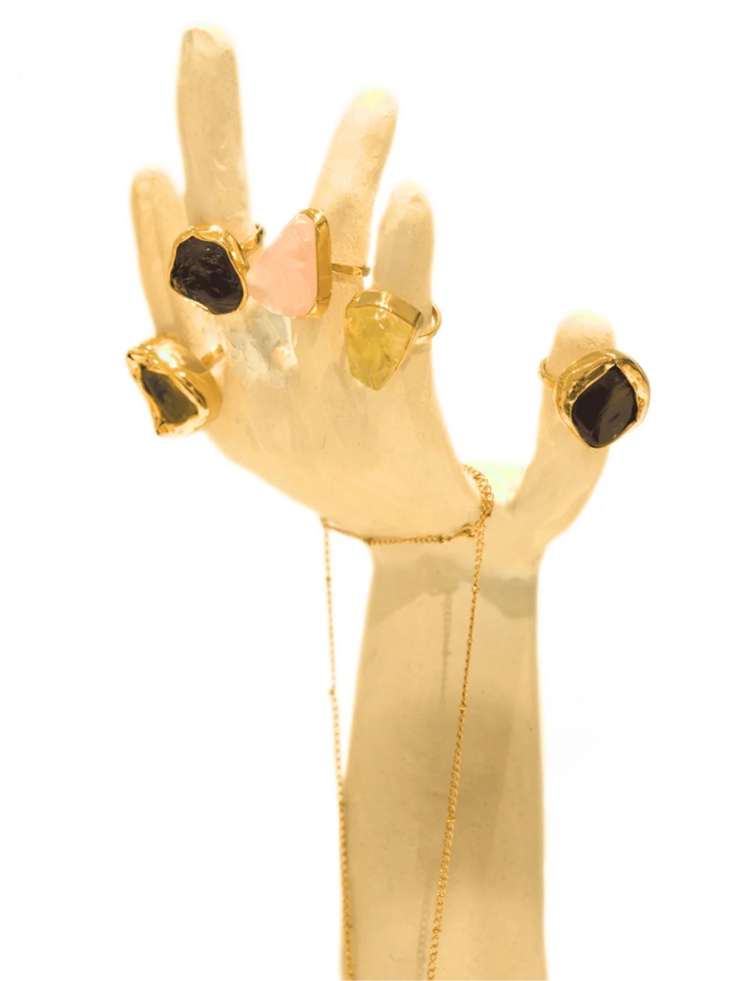 Multiple raw crystal rings in gold displayed on white hand-form prop