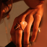 Large raw rose quartz gold ring worn on model's hand in warm side light