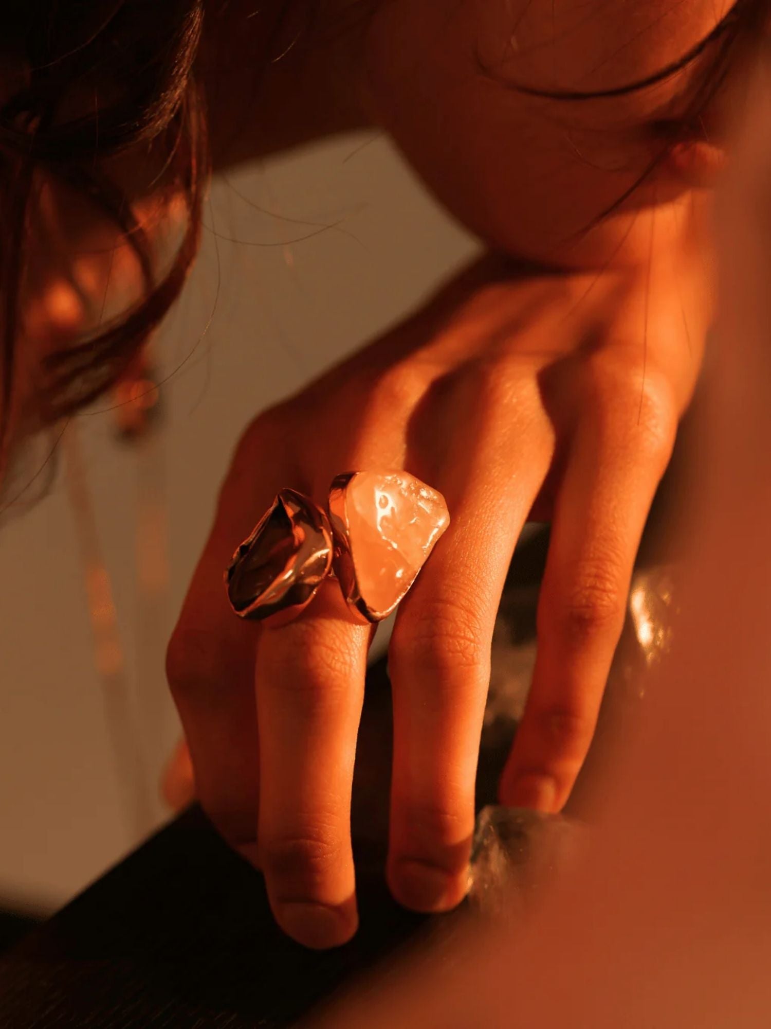 Large raw rose quartz gold ring worn on model's hand in warm side light