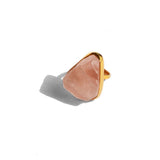 Close-up of raw rose quartz cocktail ring on model's finger in warm golden light