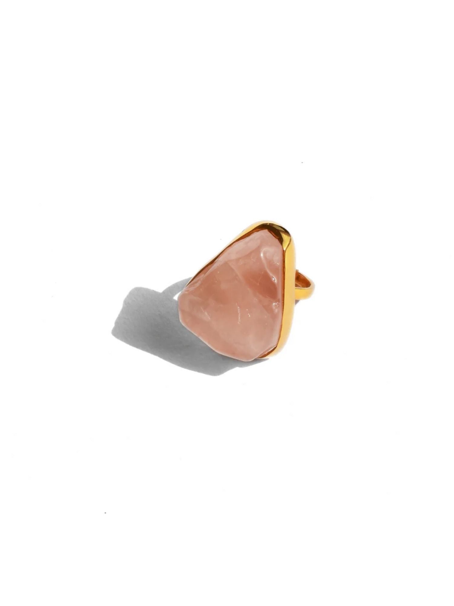 Close-up of raw rose quartz cocktail ring on model's finger in warm golden light