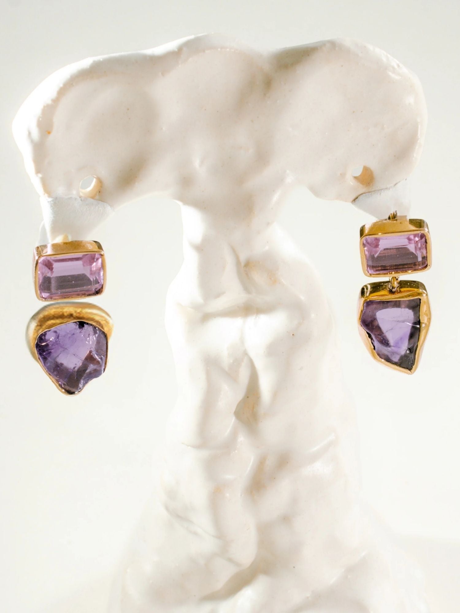 Gold and amethyst drop earrings with raw stone on white sculptural prop