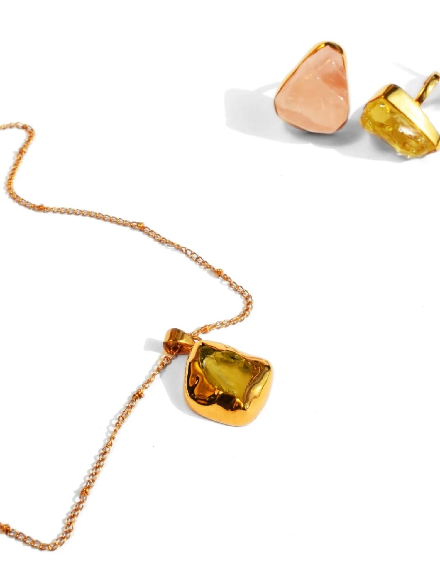 Gold pendant necklace with citrine stone and rose quartz earrings on white