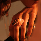 Close-up of model's hand wearing large raw rose quartz cocktail ring in warm light