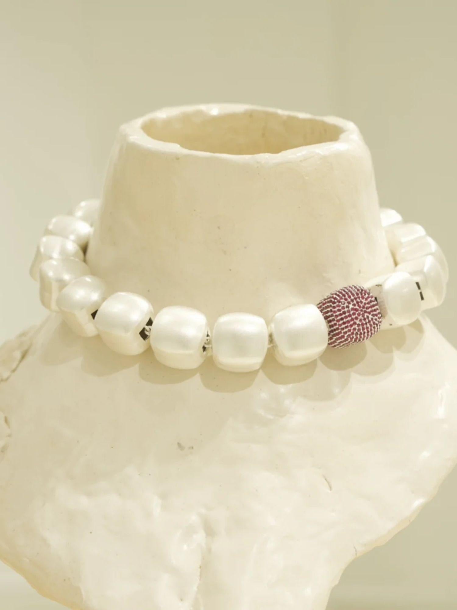 Silver cube necklace with ruby-pink CZ sphere displayed on white textured prop