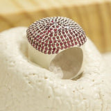 Dome-shaped cocktail ring covered in ruby-pink CZ on white textured surface