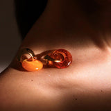 Gold amber hoop earring resting on model's collarbone in warm directional light