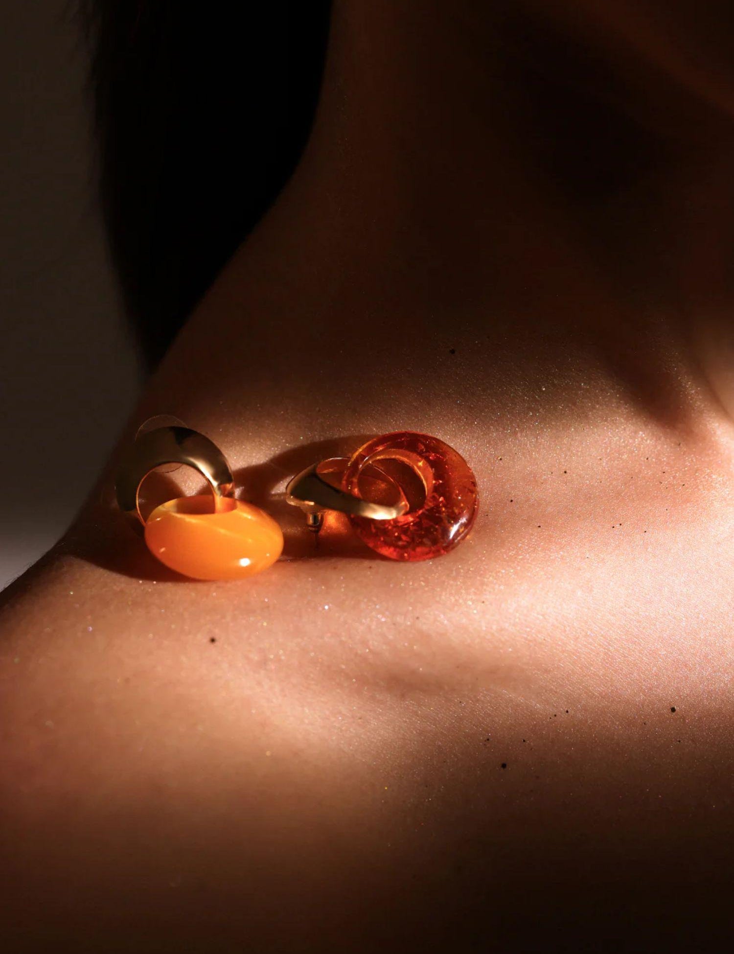 Gold amber hoop earring resting on model's collarbone in warm directional light